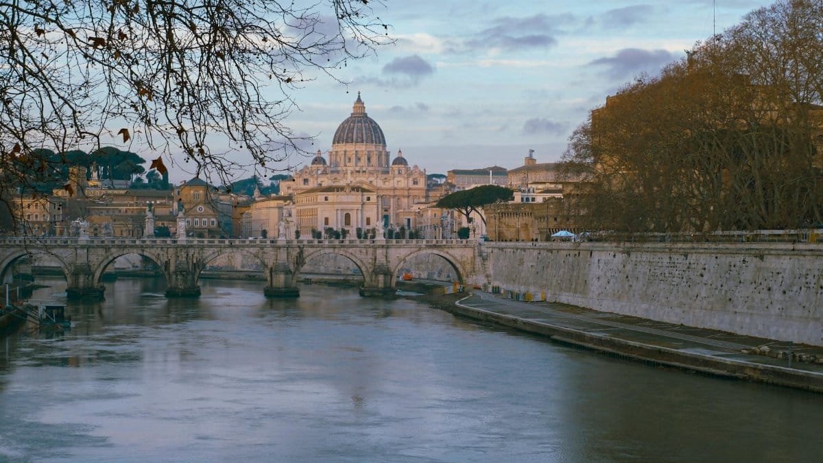 View of St. Peter's Basilica in Vatican City from across the Tiber River in Rome at sunset.