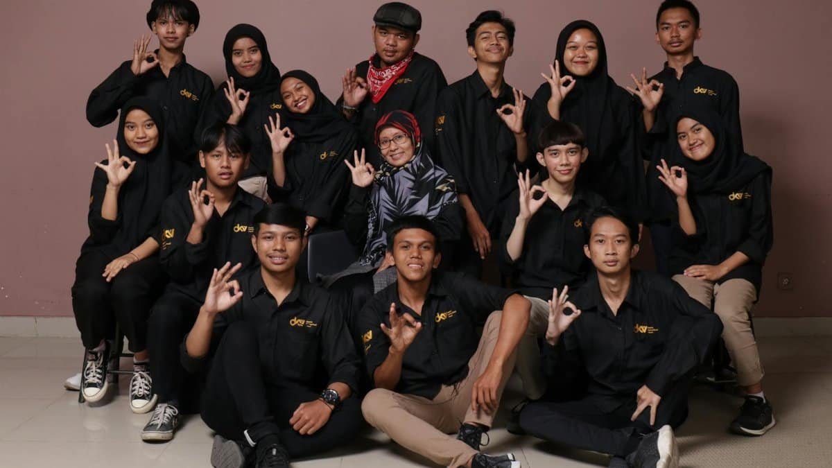 Diverse group of teenagers and a mature woman posing in black outfits, making hand signs.