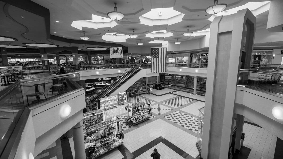 A spacious, modern indoor shopping mall with escalators and an American flag.