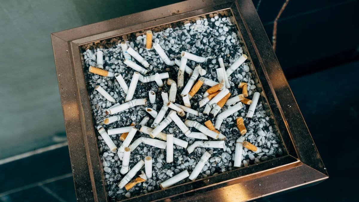 Close-up photo of cigarette butts in an ashtray filled with pebbles. Urban setting.
