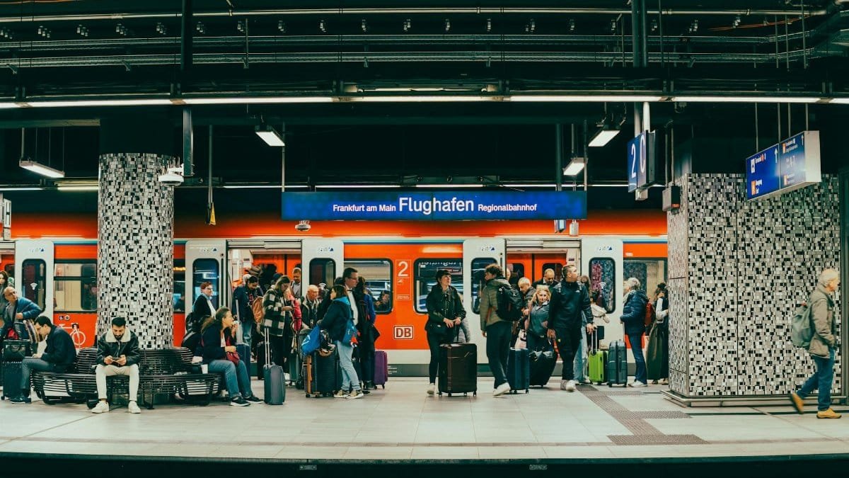 Passengers wait on the platform at Frankfurt am Main Flughafen train station with a regional train in the background.