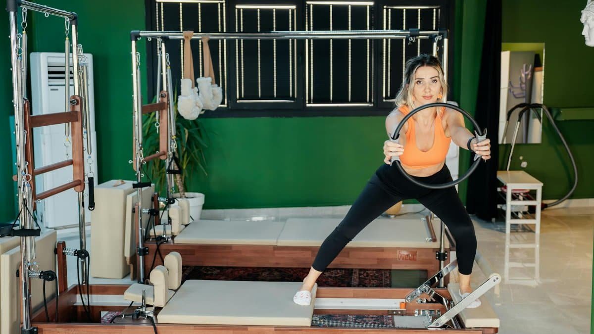 Young woman exercising on a Pilates reformer in a studio setting, showcasing strength and flexibility.