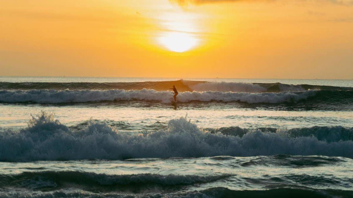 A surfer rides the waves during a vibrant sunset on a Bali beach, capturing a stunning tropical scene.