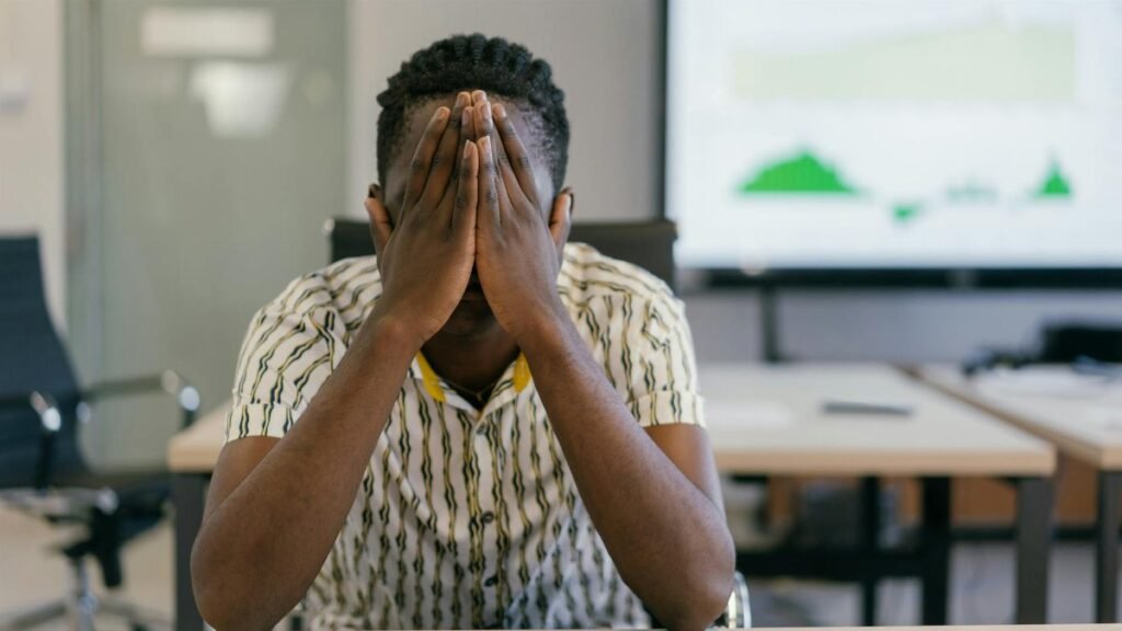 A stressed employee covering face in a modern office, depicting work pressure.