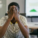 A stressed employee covering face in a modern office, depicting work pressure.