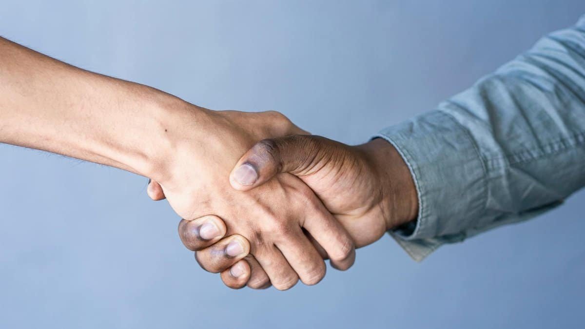 Close-up of a handshake between two people against a blue backdrop.