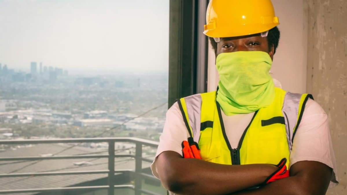 Construction worker wearing PPE in a high-rise building with city view.