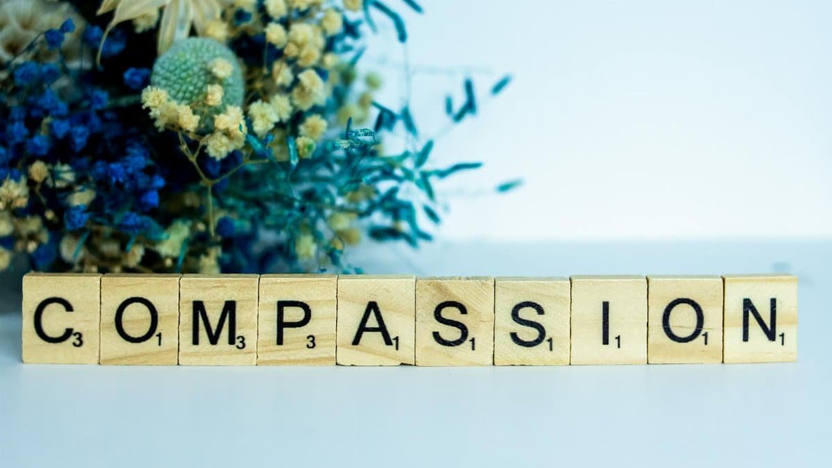 Scrabble tiles spelling 'compassion' with vibrant floral background.