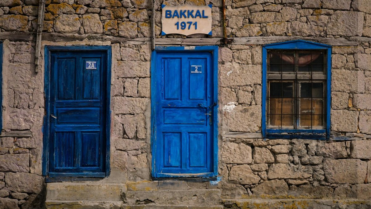 Historic stone building with vibrant blue doors and windows, marked 'BAKKAL 1971.'