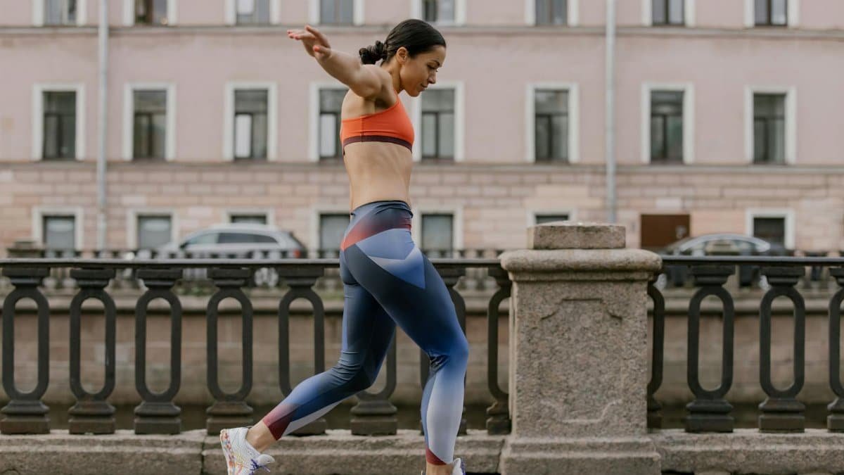 Woman in colorful activewear balancing on a sidewalk in front of a classic building.