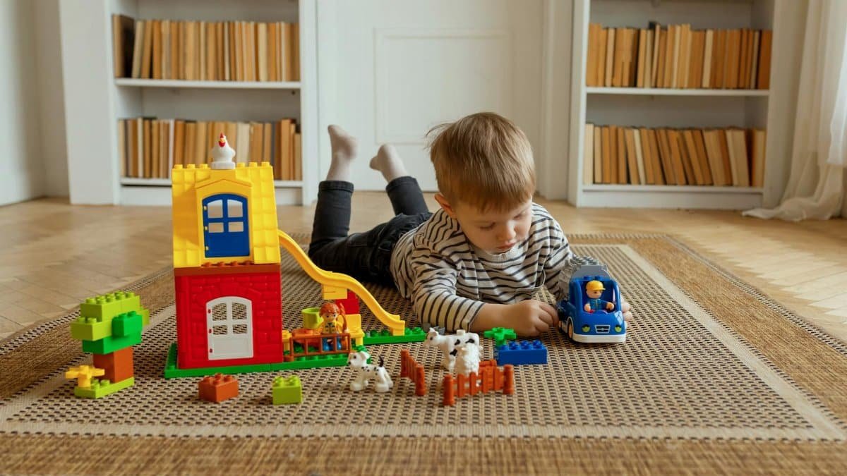 Young child playing with colorful building blocks and toy car on a woven carpet in a home setting.