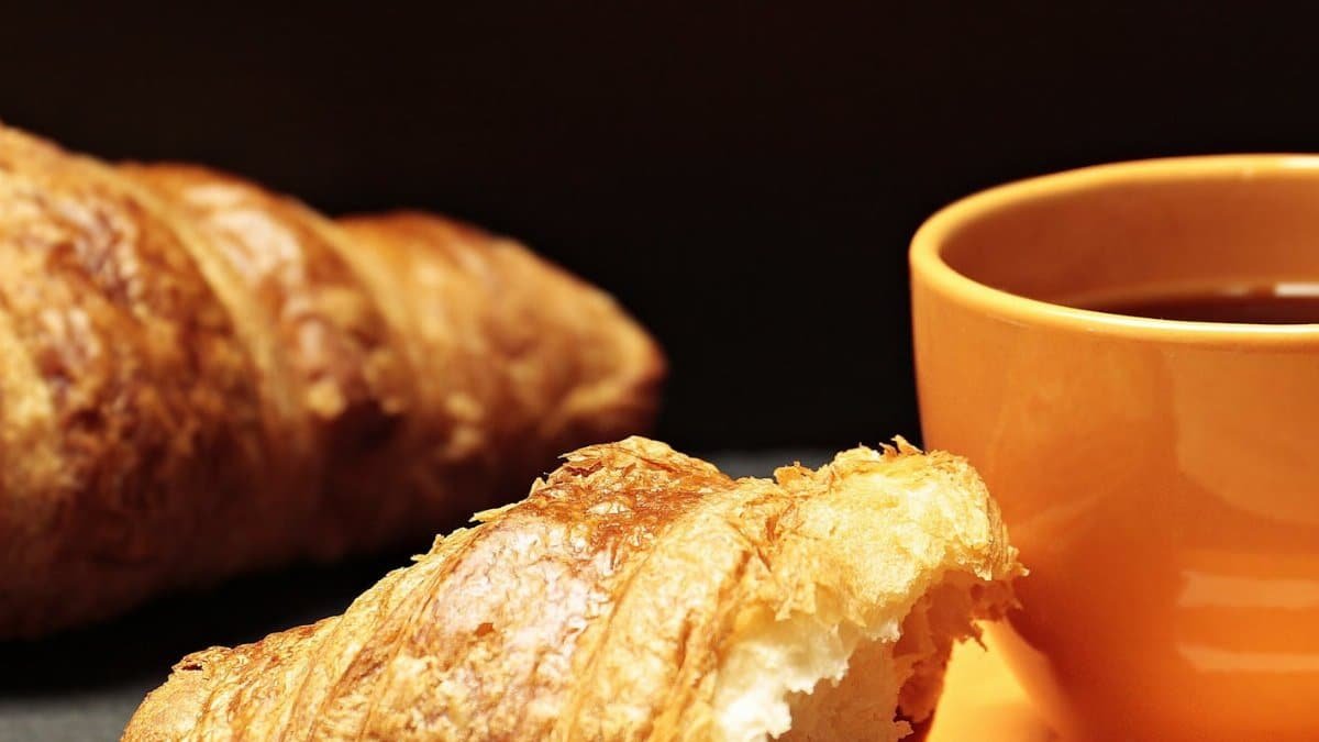 Close-up of a freshly baked croissant paired with a warm cup of coffee on a table.