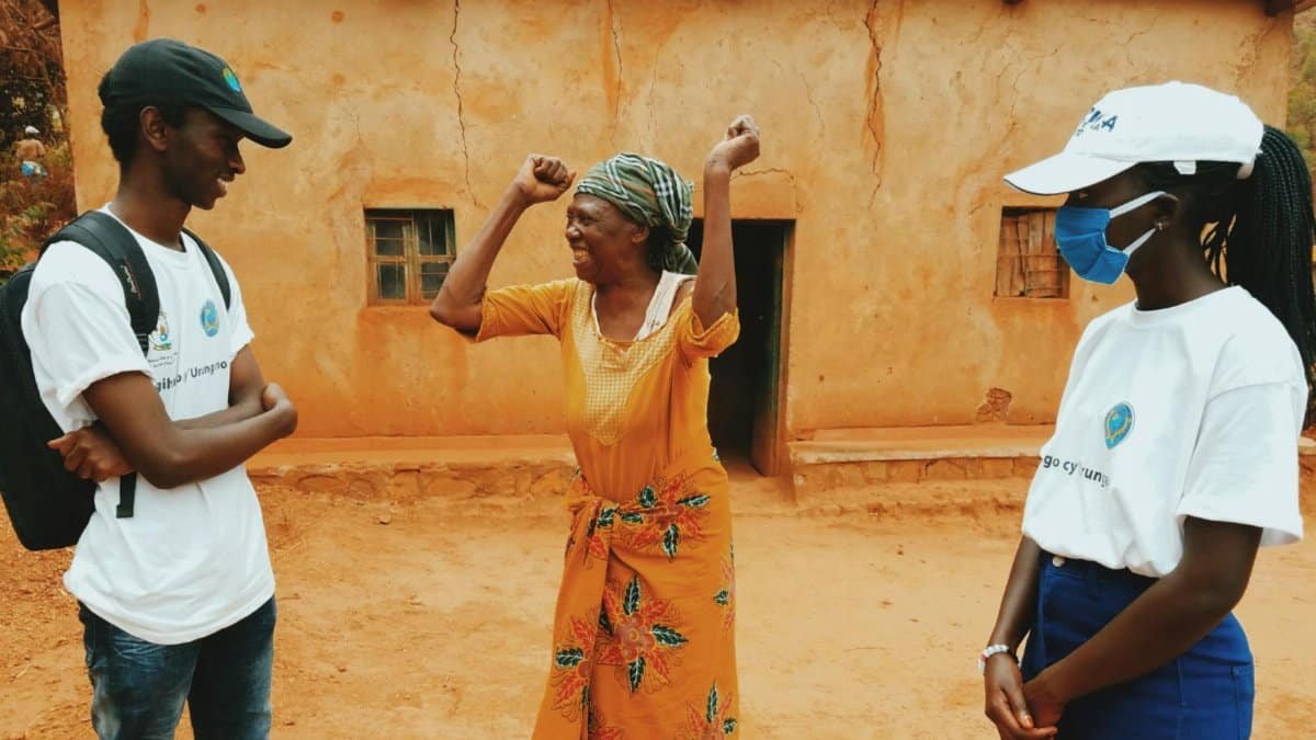 Volunteers engage joyfully with an elderly woman outside a rural home, creating community bonds.