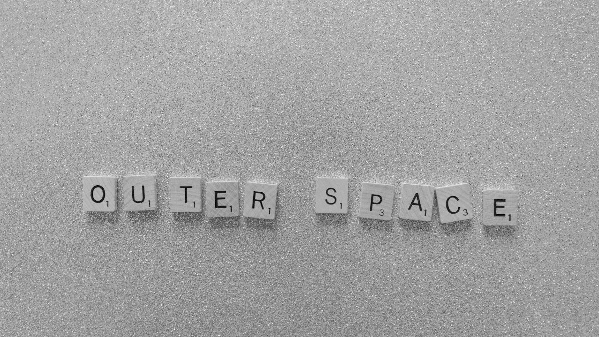 Scrabble tiles spelling 'Outer Space' on a shimmering glitter surface in black and white.