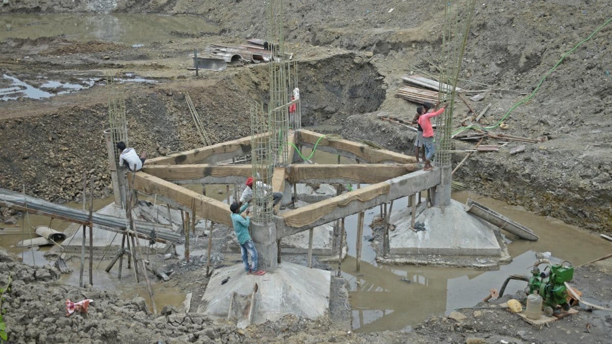 Workers constructing a building foundation with rebar and wooden supports outdoors.