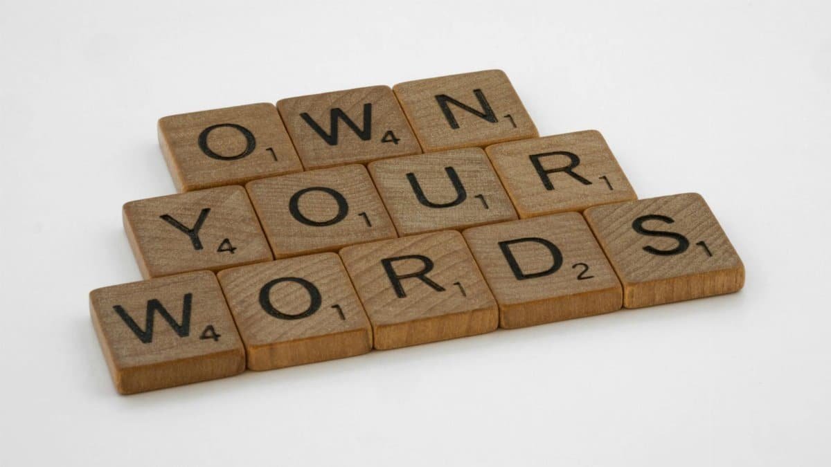 Wooden Scrabble tiles spelling 'Own Your Words' on a white background, symbolizing communication integrity.
