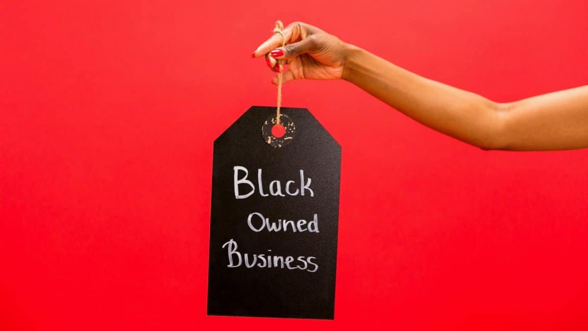 A hand holding a Black Owned Business sign against a vibrant red background, symbolizing support and diversity.