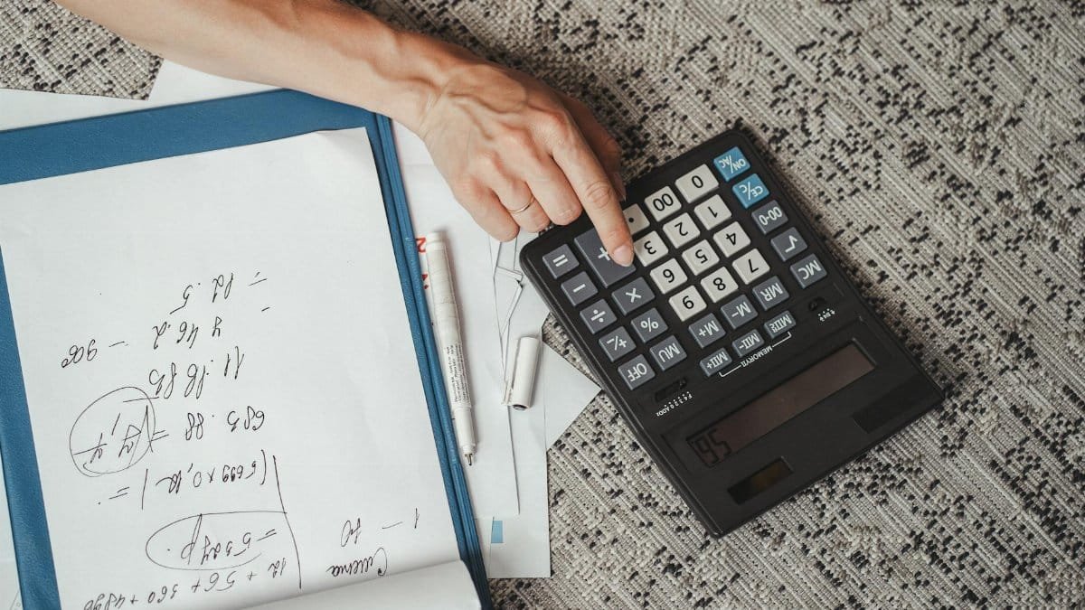 Top view of a hand calculating numbers with a large calculator and notes on a desk.