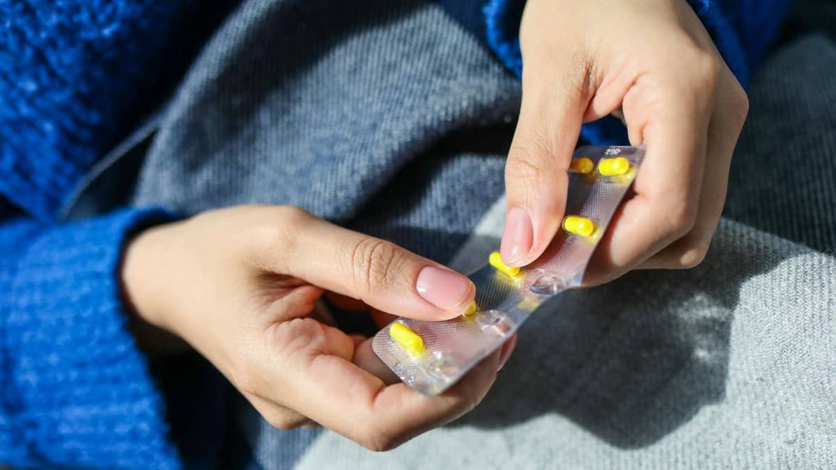 Close-up of a woman's hands holding a blister pack with yellow pills, indoors.
