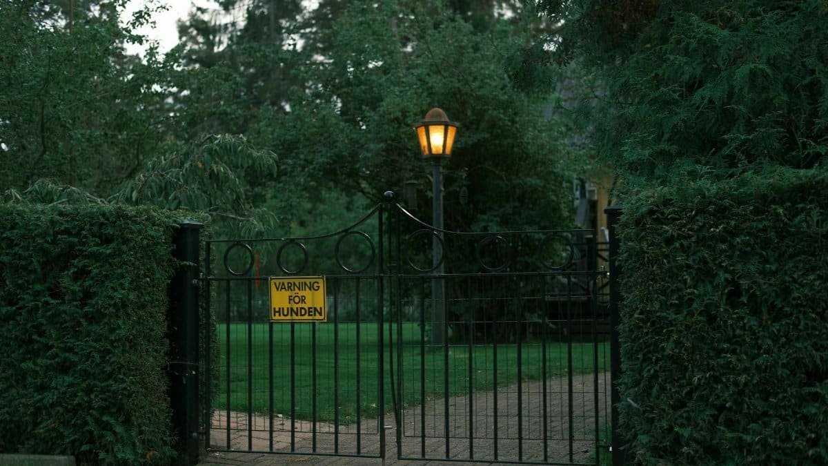 A peaceful garden entry with a warning sign, lit by a warm lamp, captured at dusk.