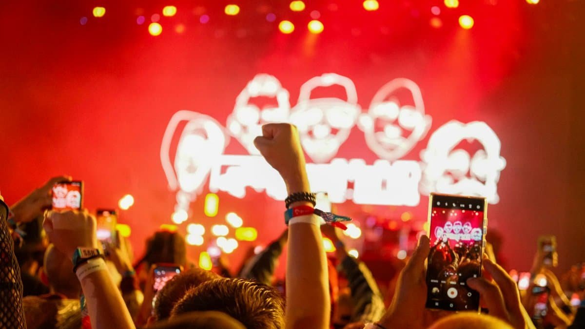 Vibrant concert atmosphere with fans capturing the stage on smartphones with raised hands.