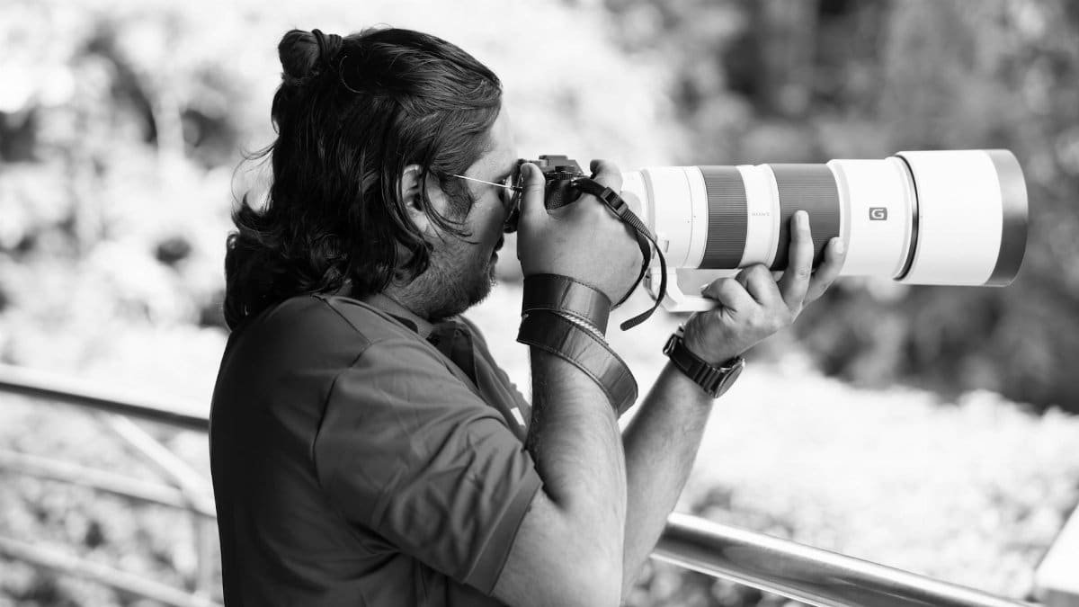 A photographer captures distant subjects with a telephoto lens outdoors, in black and white.