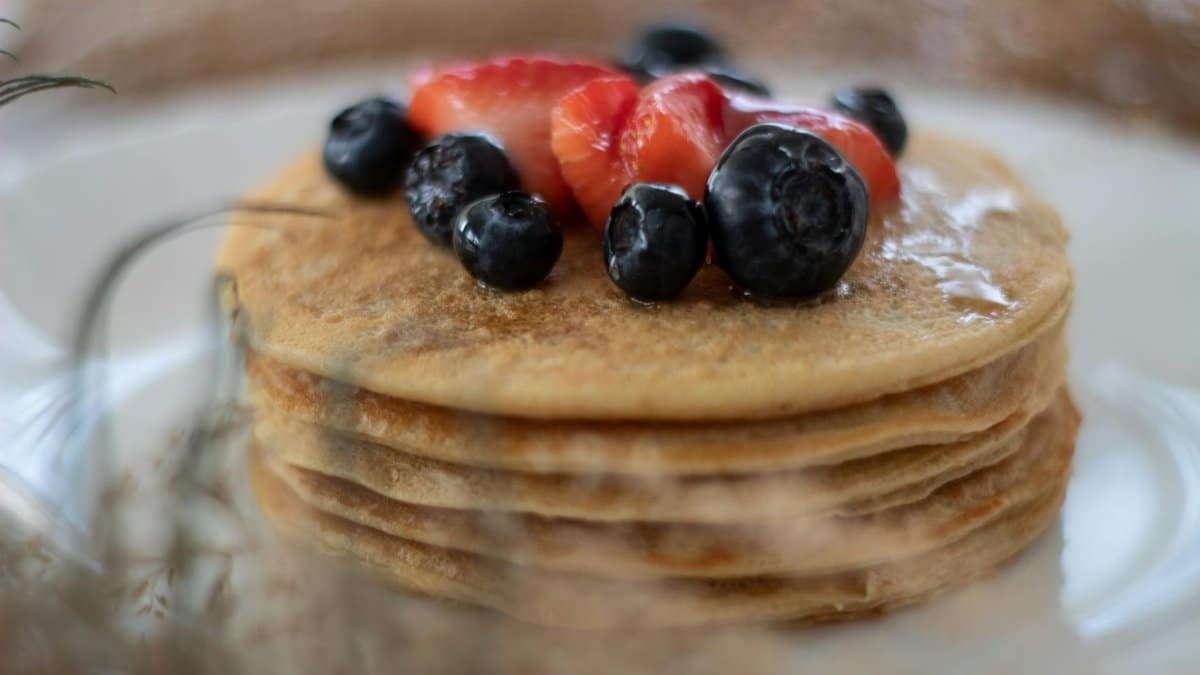 Close-up of a stack of pancakes topped with strawberries and blueberries.