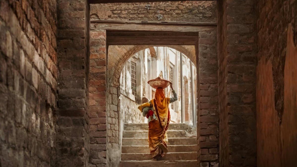 A woman in traditional attire carrying goods in a historic town's stone passageway.
