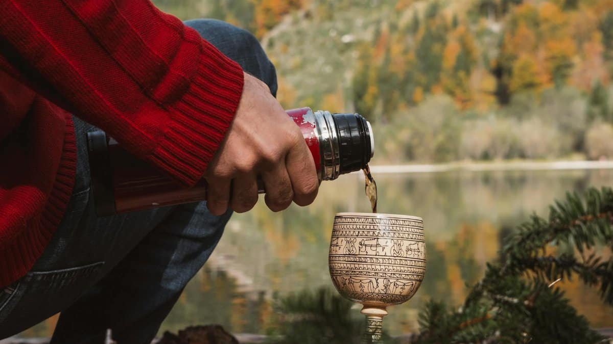 A serene autumn scene in Styria, Austria, with a cozy moment by the lake, featuring hand pouring hot drink.