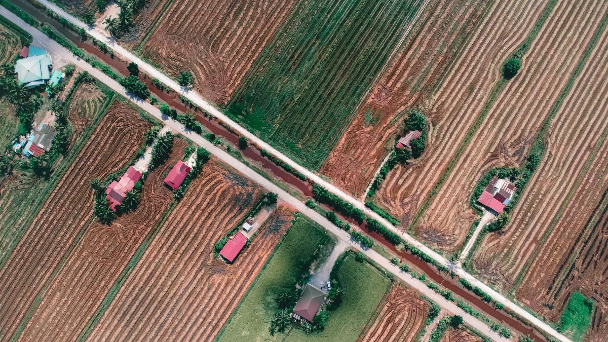 Drone shot capturing rural farmland with red-roofed houses and roads, showcasing agricultural patterns.