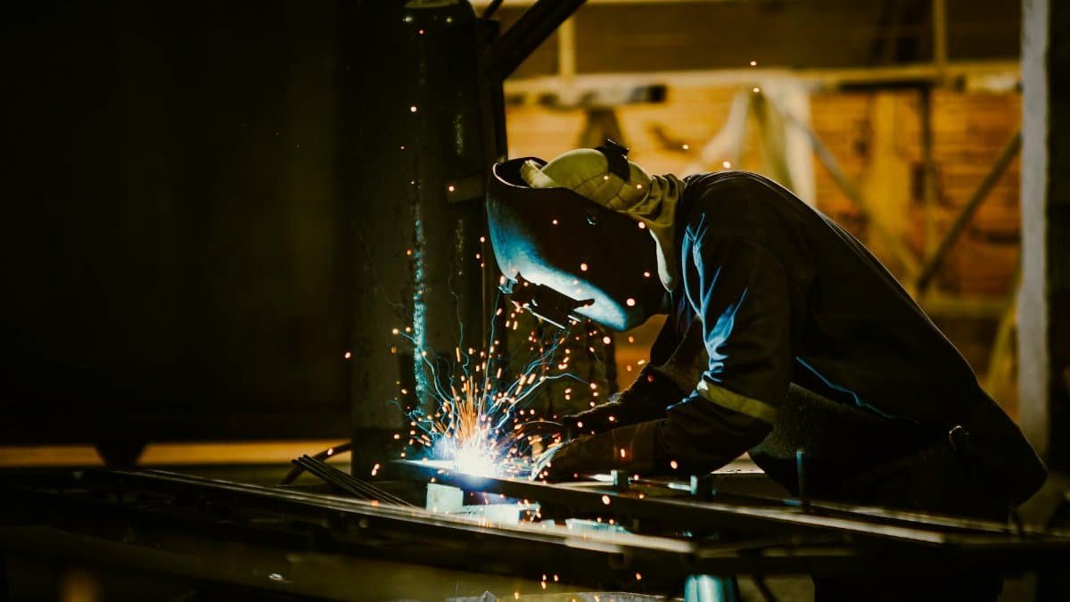 A welder in protective gear works in an industrial setting, with sparks illuminating the scene.