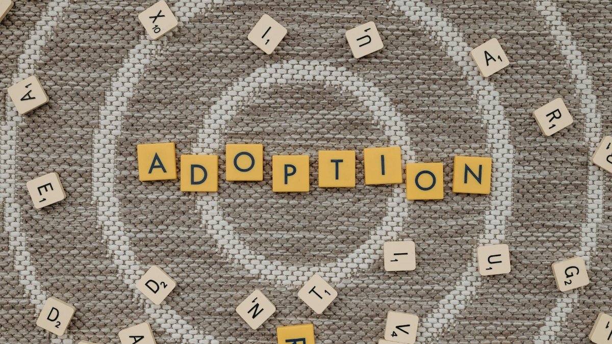 Top view of scrabble letters spelling 'adoption' surrounded by random letters on a patterned surface.