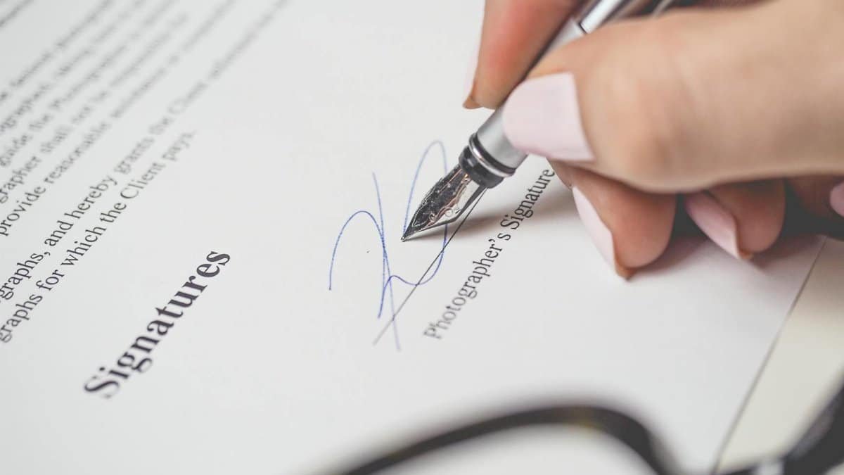 Close-up of a hand signing a contract, showcasing a pen and elegant handwriting.