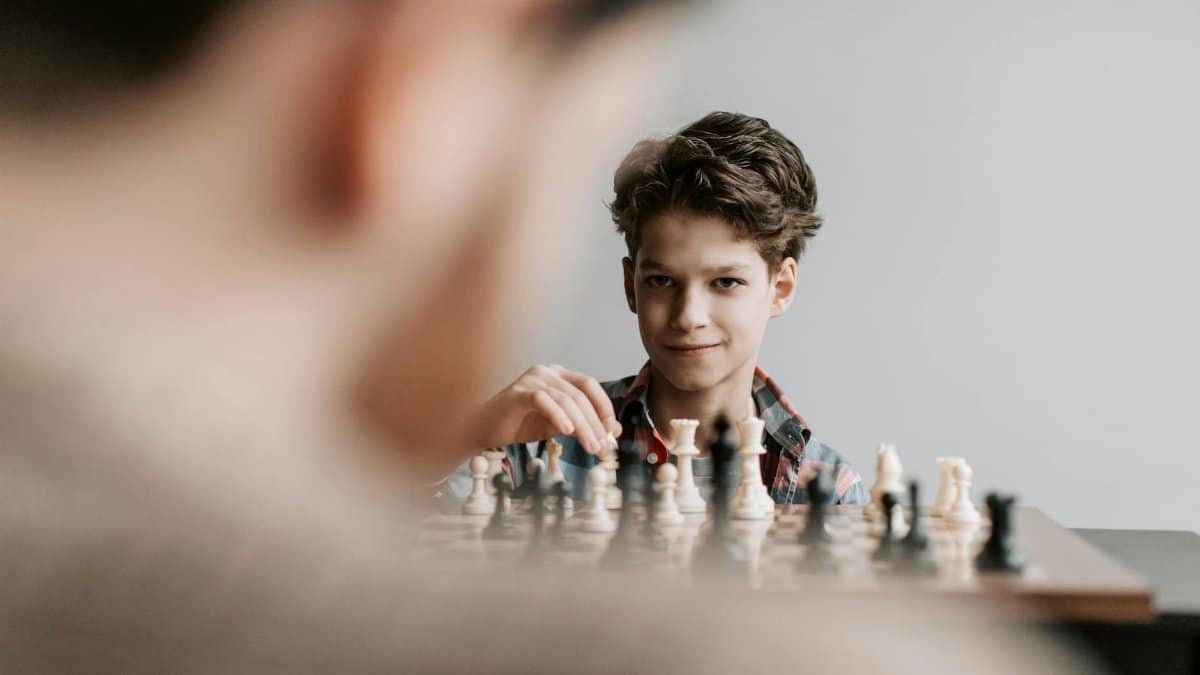 A young boy plays chess indoors, focusing intently on the chessboard.