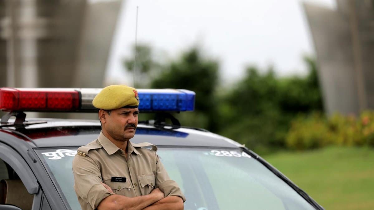 Indian police officer with arms crossed standing by a patrol car outdoors, showcasing authority and law enforcement presence.