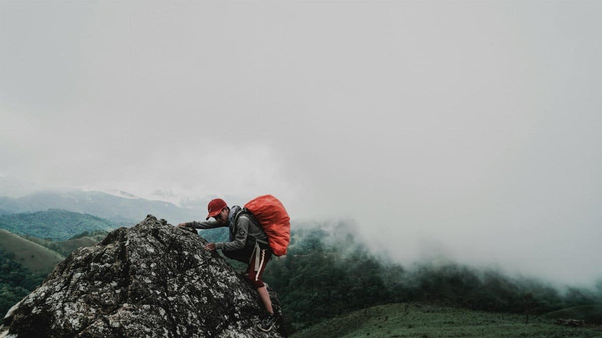 A determined hiker ascends a rocky mountain in foggy weather, showcasing endurance.