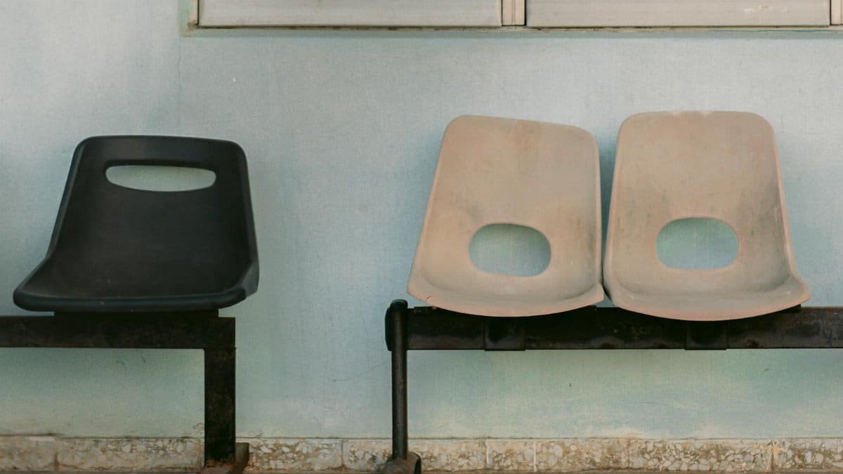 An empty waiting room bench with one black and two beige chairs against a blue wall.