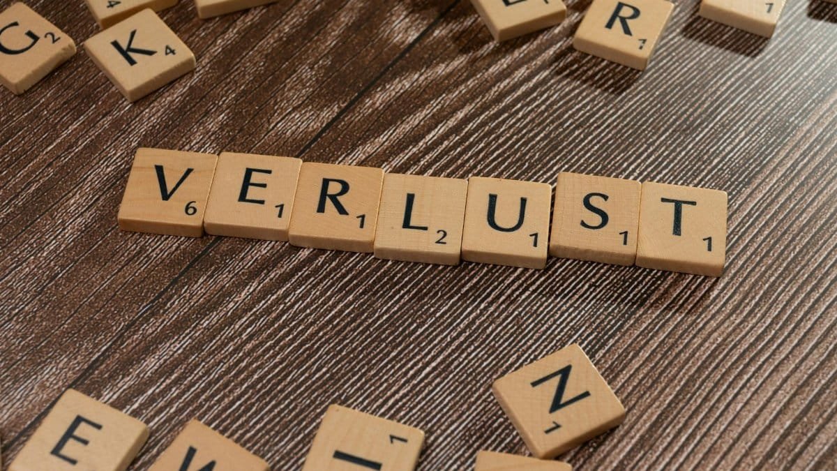 Scrabble tiles spelling 'Verlust' on a wooden table, symbolizing loss or financial context.