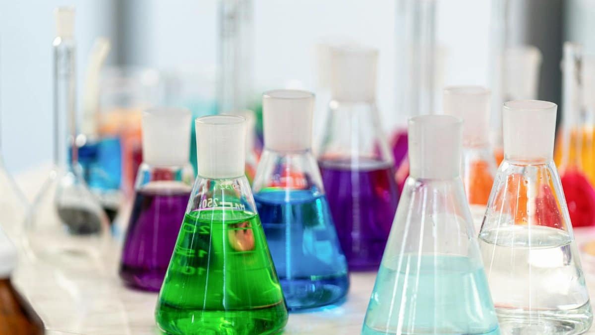 Close-up of colorful chemical solutions in glass beakers in a laboratory setting.