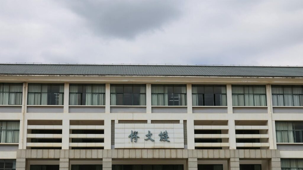 Front view of a modern educational building with Asian architectural elements under a cloudy sky.