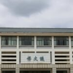 Front view of a modern educational building with Asian architectural elements under a cloudy sky.