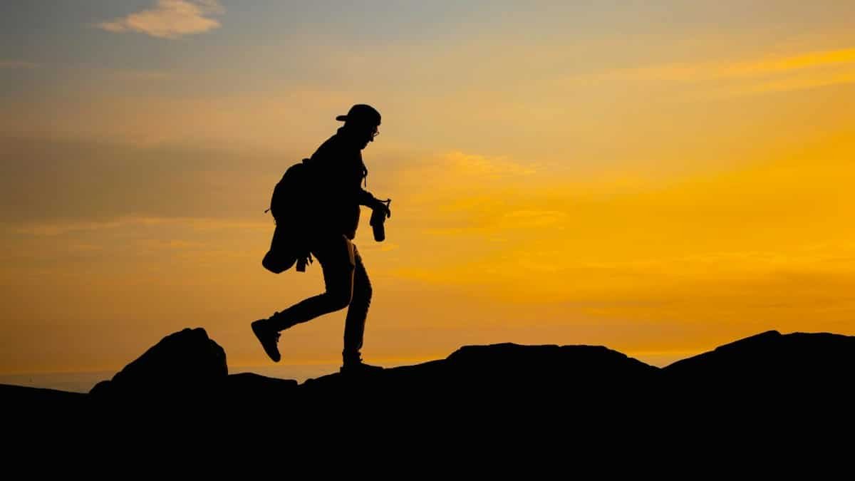 A dramatic silhouette of a man hiking over rocks at sunset, capturing outdoor adventure.