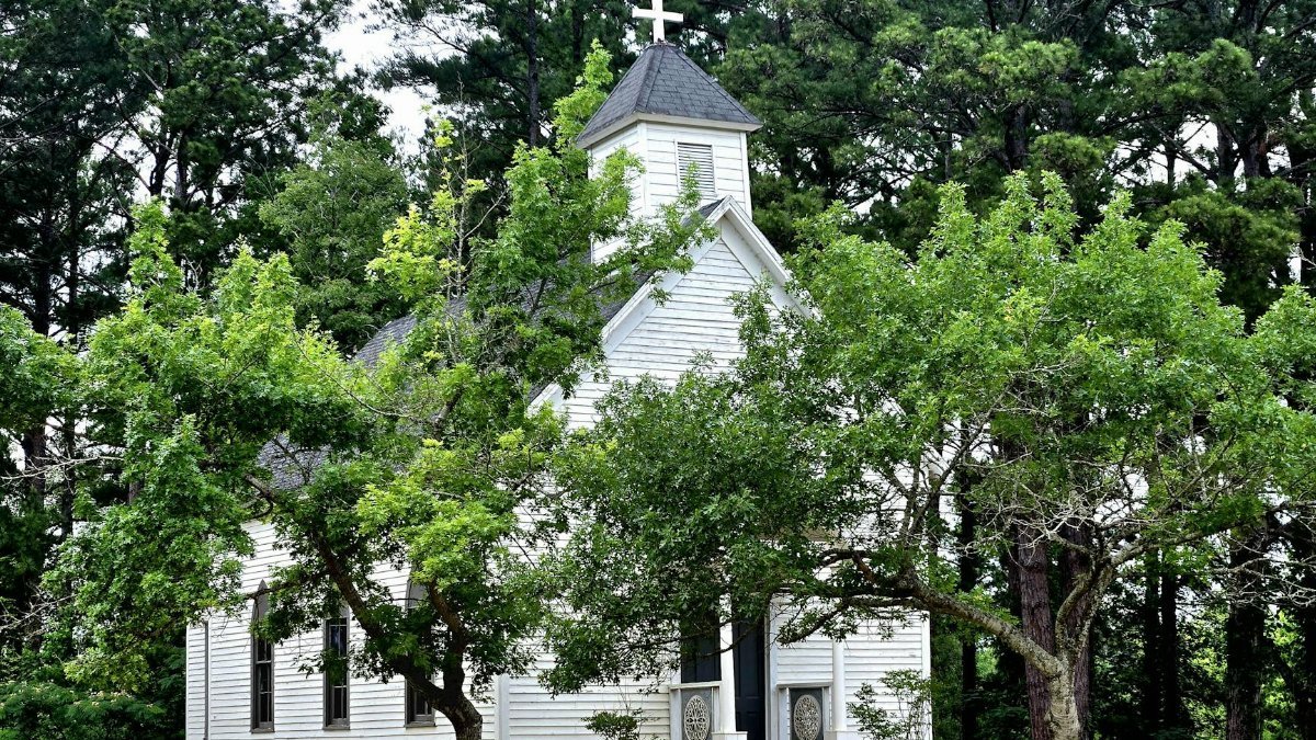 A quaint white church with a steeple surrounded by lush green trees, exuding a serene atmosphere.