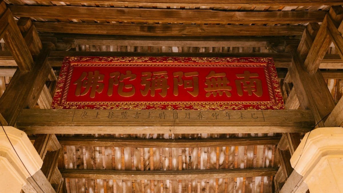 View of a traditional wooden roof structure with an intricate red and gold sign, photographed from below.