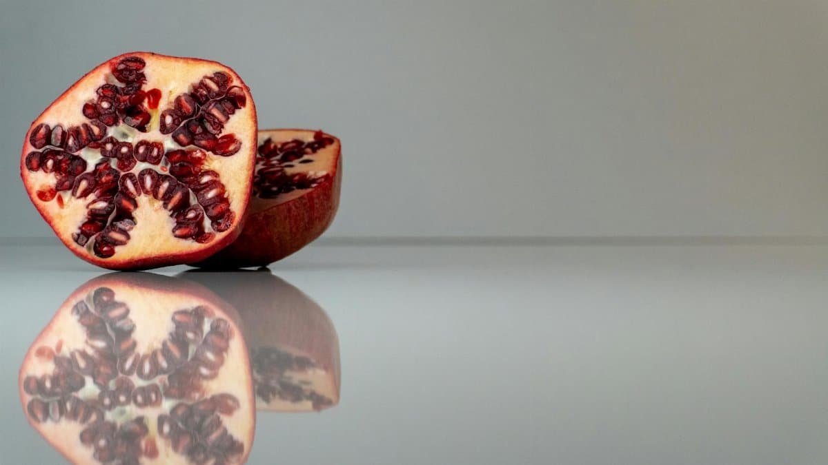 Close-up of fresh pomegranate halves on a reflective surface, showcasing vibrant seeds.