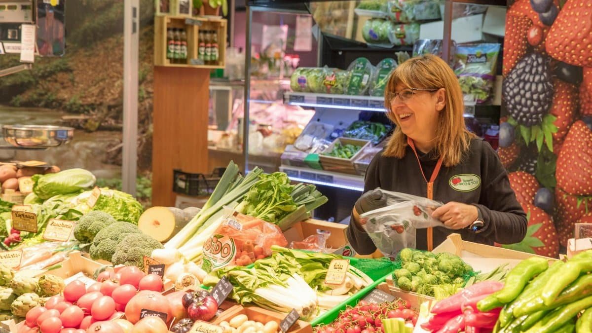 Cheerful woman selling fresh produce at a vibrant market stall. Ideal for promoting local grocery shopping and healthy eating.