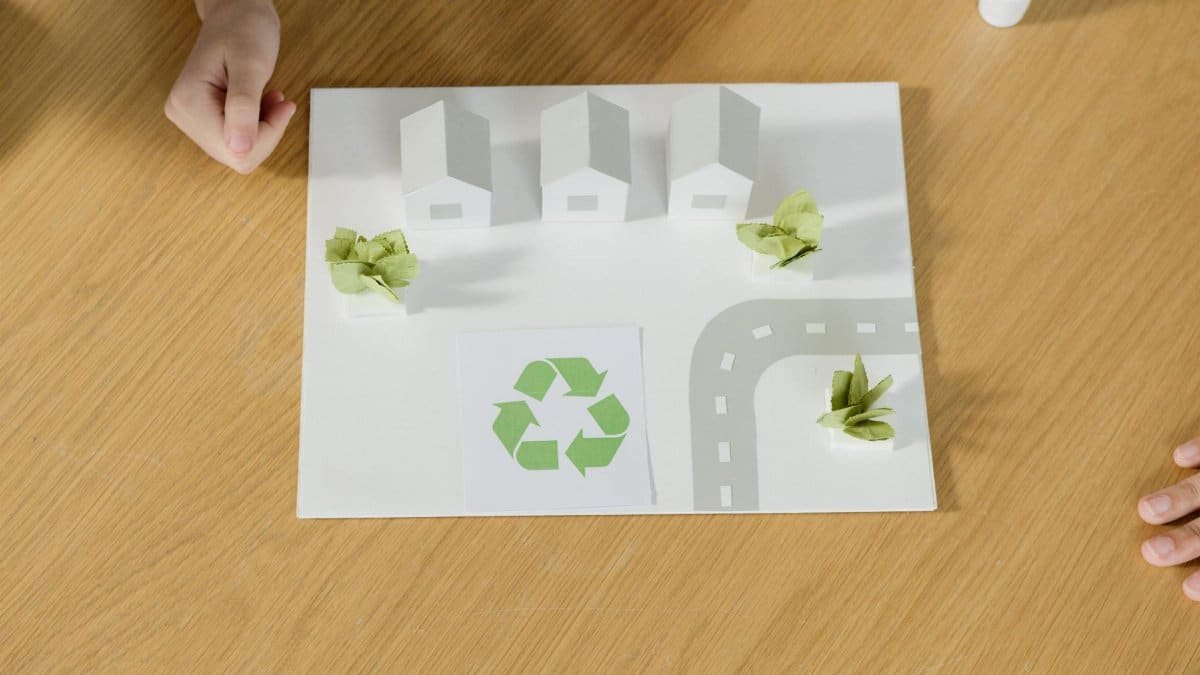 A paper model of a sustainable community featuring houses and recycling symbol, emphasizing eco-friendly living.