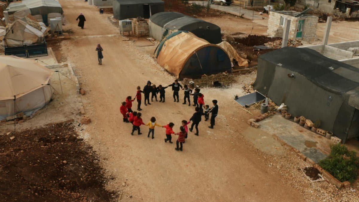 Children play together in a circle at a Syrian refugee camp, capturing a moment of joy and camaraderie.