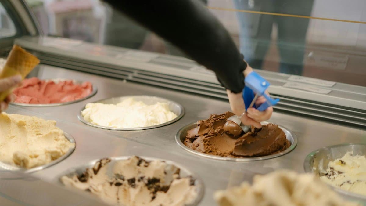 A hand scoops chocolate ice cream in a vibrant gelato shop in Perth, Australia. Indulge your sweet tooth.