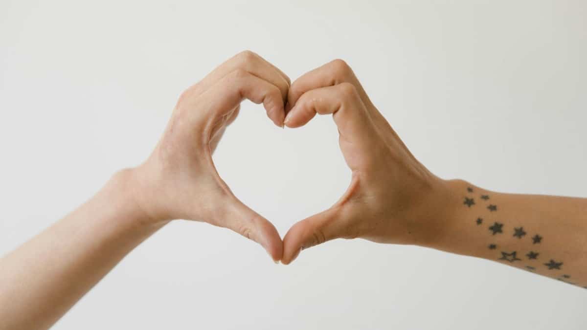 Two hands form a heart shape on a white background, one with star tattoos.
